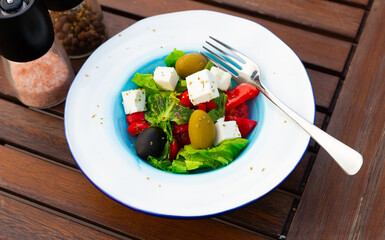 Organic greek salad with feta, olives, vegetables and tomato on the wooden table in a cafe