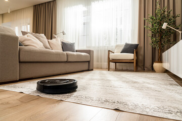 Panorama of a black robot vacuum cleaner in a new living room in light beige and gray colors