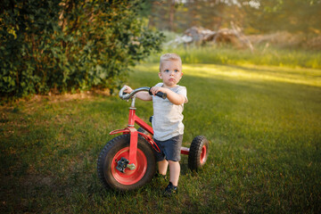 Boy standing with a red trike in the summer time