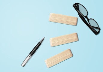 Wooden block on blue background with black glass and pen.