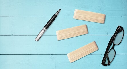 Wooden block on blue background with black glass and pen.
