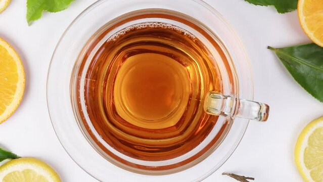 different types of fresh raw green tea leaf flower bud lemon orange slice transparent glass teacup saucer liquid tea on white background top view pan zoom rotate