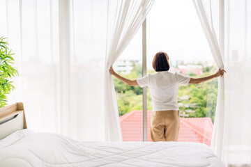 Fototapeta na wymiar Smiling of happy young beautiful pretty asian woman waking up and opening window curtains.Girl feeling comfortable and relaxed breathing fresh air in morning in bedroom at home