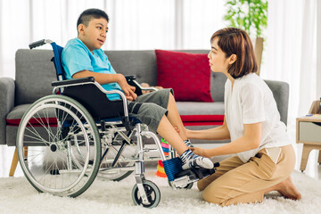 Naklejka premium Portrait of enjoy happy love family asian mother playing and carer helping look at disabled son child sitting in wheelchair moments good time at home.disability care concept 