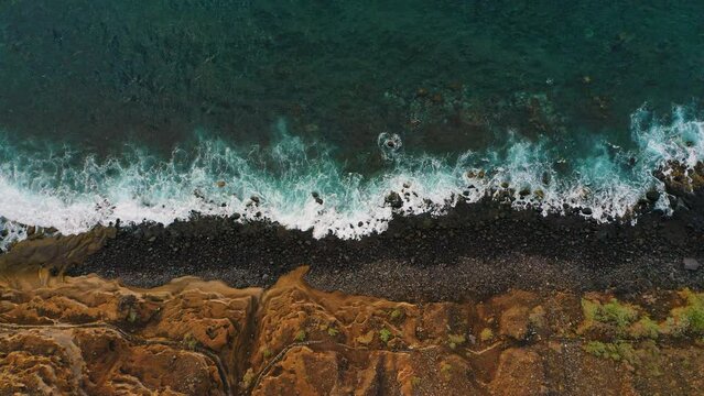 Aerial drone top down view of coastal cliffs and rocky beach in twilight, sunset. Blue ocean water. Amazing sea waves foam crashing on the volcanic stones, rock. Seascape. Tenerife. Canary Island.