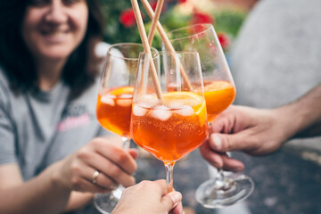 Friends raise glasses of Venetian Spritz at a home party. Front view.