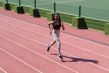 Young black sportswoman enjoys running on red track around stadium to improve technique and increase endurance. African American woman with long braids prepares for upcoming marathon on hot summer day