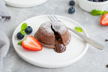Chocolate fondant lava cake with fresh berries on a plate on a gray background.