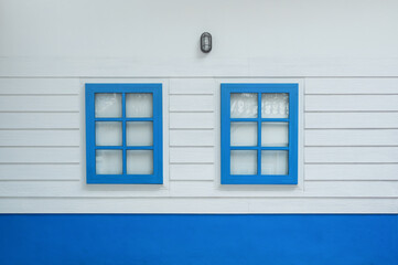 Two windows on white wood wall, outdoor view. Colorful blue window from front outside of house.