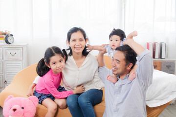 Fototapeta premium Selective focus Asian happy family laughing and hugging with love and warmth, smiling parents and eldest sister with toddler having fun together in holiday, family enjoying free time.