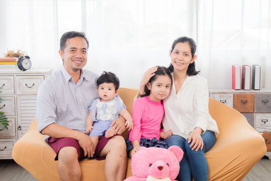Selective focus Asian happy family sitting on cozy sofa cuddling with two little children take a photo in living room. Sibling with mom and dad spend time together in holiday, family enjoy free time.