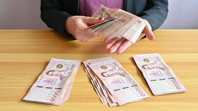 An accountant woman sitting and holding a pile of Thai baht banknotes. The baht is the official currency of Thailand.