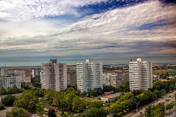 Fototapeta na wymiar Three sixteen-story houses in the city from a height under a blue sky with clouds among the trees