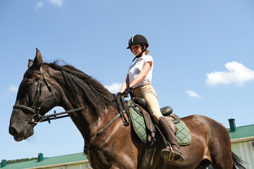 A young girl on a brown horse is engaged in show jumping outdoors.
