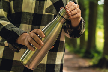 Close-up of Unrecognizable female hand holding Water bottle. Reusable steel thermo water bottle in...