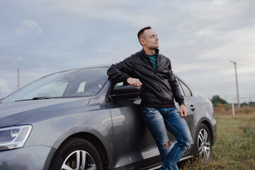 Handsome stylish man standing near his car at the field
