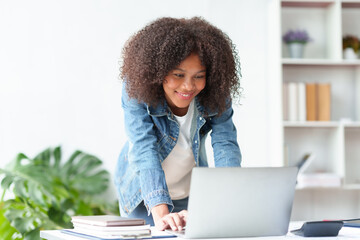 Smiling beautiful business woman happily and comfortably working on her laptop computer and taking notes and working on paperwork at the office..