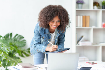 Smiling beautiful business woman happily and comfortably working on her laptop computer and taking notes and working on paperwork at the office..