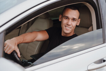 Happy young driver sitting in his car with smile