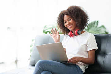 Beautiful young woman student sitting on sofa is video chatting on laptop, smiling faces and gestures happily studying.