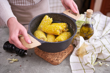 Cooked corn cobs in pot on grey concrete table