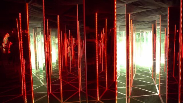 Mirrors flicker in the maze. Beautiful girl in infinity mirror maze. Amusement park. Mirrors distort reality. Young woman in metaverse. Interactive room with colorful fluorescent tube illumination.