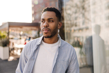 Modern young african man looking away spending leisure time outdoors. Brunette guy wears casual clothes. City life concept