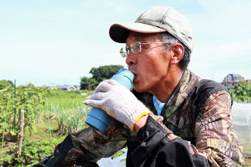 畑で水分補給するシニア男性