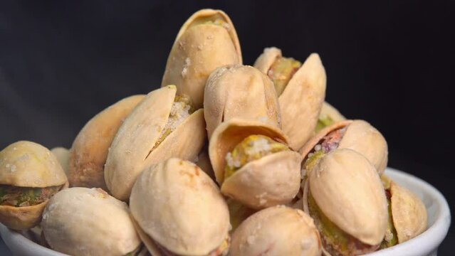 Hot roasted pistachios rotate in a bowl on a black background. Salted pistachio nuts for beer background close up. Vegan Healthy food high protein. Dietary nutrition. Concept of nuts.
