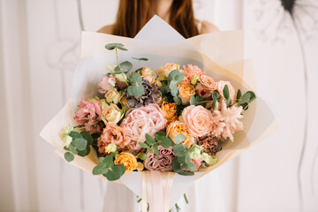 Very nice young woman holding big and beautiful bouquet of fresh roses, carnations, eustoma, peonies, eucalyptus in peach colors, cropped photo, bouquet close up