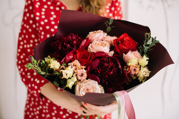 Very nice young woman in a polka dot dress holding big and beautiful flower bouquet of fresh eustoma, roses, peonies, eucalyptus in cream and red colors, cropped photo, bouquet close up
