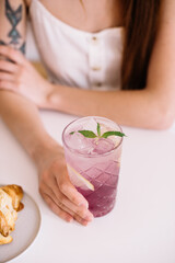 Very nice young woman holding glass of purple lavender lemonade, close up vertical view