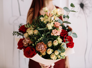 Very nice young woman holding big and beautiful bouquet of fresh roses, carnations, eucalyptus, eustoma flowers in cream and red colors, cropped photo, bouquet close up