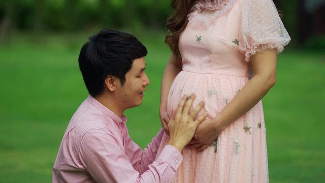 married couple is expecting a baby. man kissing belly of his pregnant wife in the park
