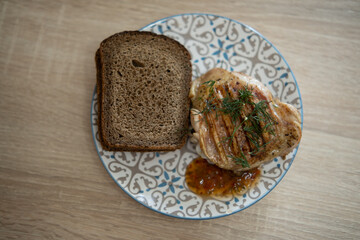 Grilled chicken steak with sauce and bread on a plate on the kitchen table