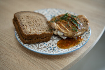 Grilled chicken steak with sauce and bread on a plate on the kitchen table