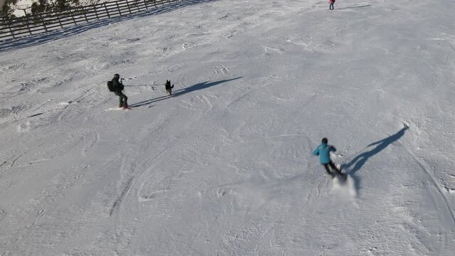 High view of a dog at a ski site while its owner holds his leash and goes skiing with people passing by, in Navacerrada, Madrid, Spain