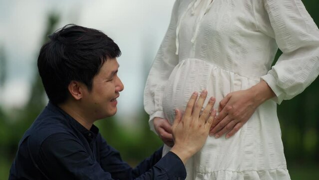 married couple is expecting a baby. man kissing belly of his pregnant wife in the park