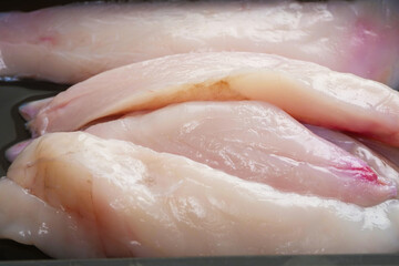 Raw uncooked monk fish portion fillet on a black plastic tray. White isolated background. Top...