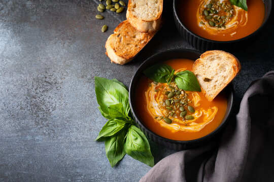 Pumpkin soup with bread, seeds and basil leaf on dark background