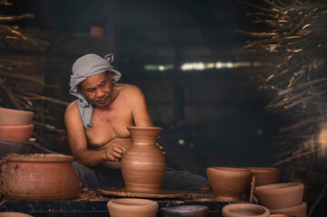 A senior man is using a potter's wheel to make pottery from wet clay.