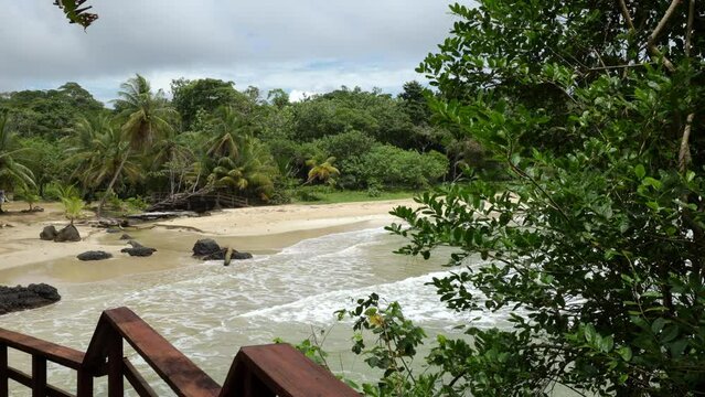 Panning shot of a wooden walkway with railing and a paradise beach in the background
