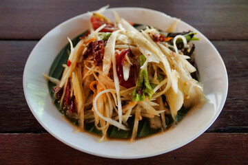 Close-up to papaya salad in a small plate on a wooden table