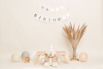 Teddy bear with party cone sitting near little wooden bench on background with happy birthday...