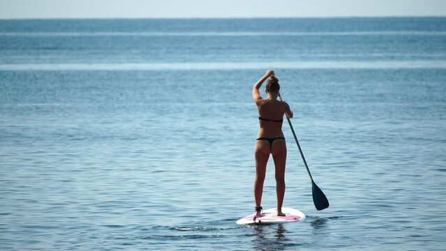 Sea woman sup. Silhouette of happy young woman standing, surfing on SUP board, confident paddling through water surface. Idyllic sunset or sunrise. Active lifestyle at sea or river. Slow motion