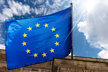 Close-up of a European Union flag waving against a clear blue sky with clouds and sunbeams. Brescia, Lombardy, Italy, Europe.