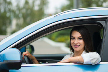 Adult black-haired woman driver sits in blue car. Stylish businesswoman enjoys successful life smiling. Happy lady grimaces in leather cabin closeup