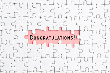 White jigsaw puzzle with congratulations word over pink background.