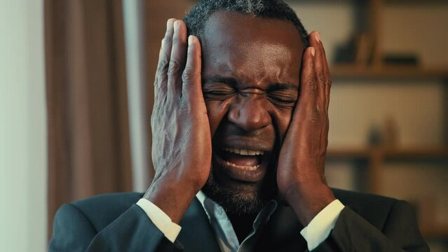 Close-up annoyed excited african american man covering ears with hands over noise feeling panic attack screaming suffering from headache depressed businessman experiencing problem feels rage pain