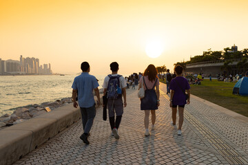 youngsters students boy and girl chat and walk during sunset in West Kowloon Waterfront Promenade, Hong Kong in evening. back light shot
